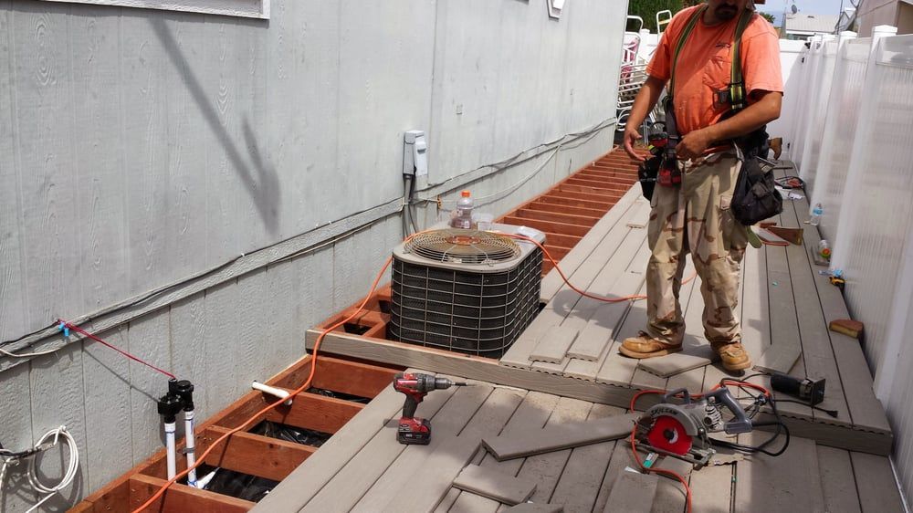 Construction worker installing deck boards. Beige deck, wooden beams, power tools, near a house.