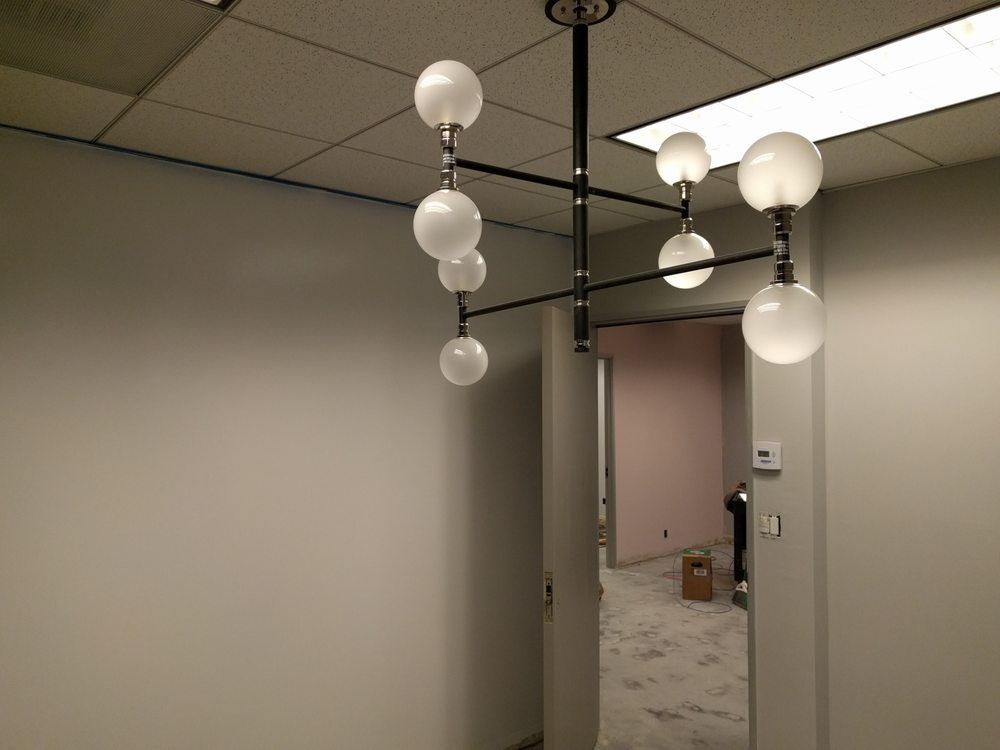 Modern chandelier with white globes in a room with pale walls and a doorway.