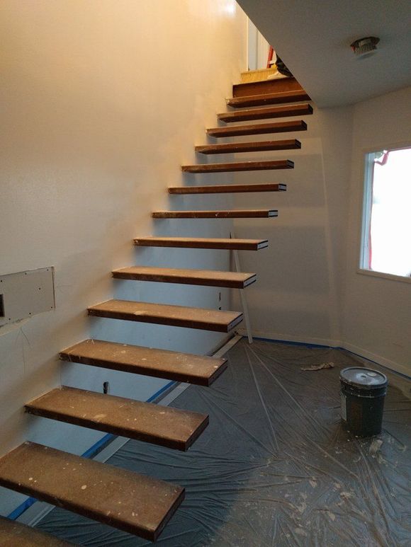 Wooden floating stairs against a white wall, ascending to the right. A bucket and window are visible below.