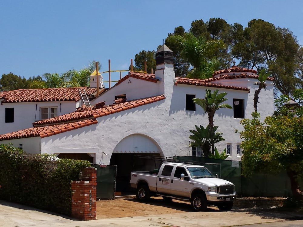 White stucco home with orange tile roof, arched entrance, and pickup truck parked in driveway.