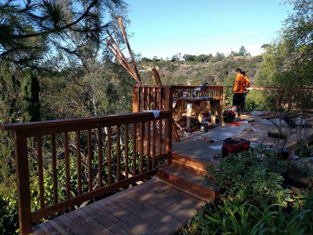 Wooden deck overlooking a lush valley, person in orange shirt working, blue sky.