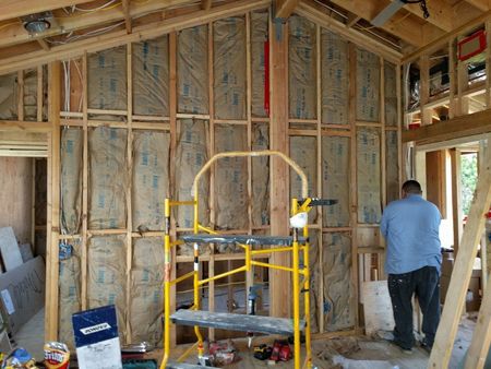 Interior of a building under construction, insulated walls, with a person working, yellow scaffolding.