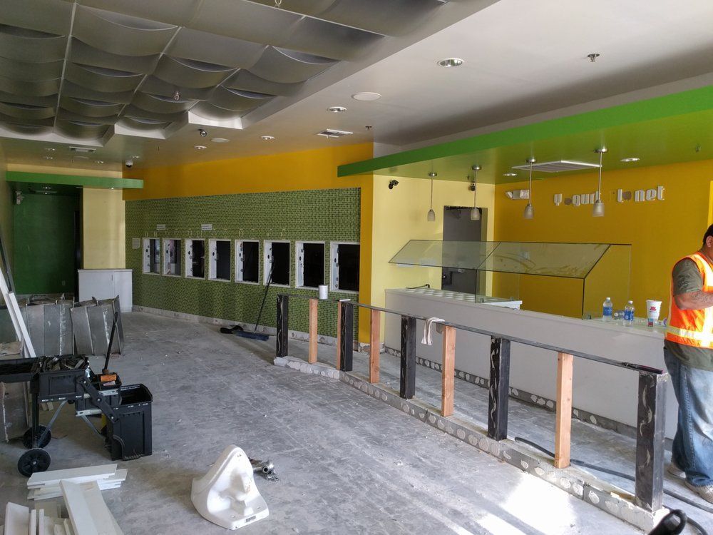 Interior of a business under construction. Yellow and green walls, long counter, worker in a vest.