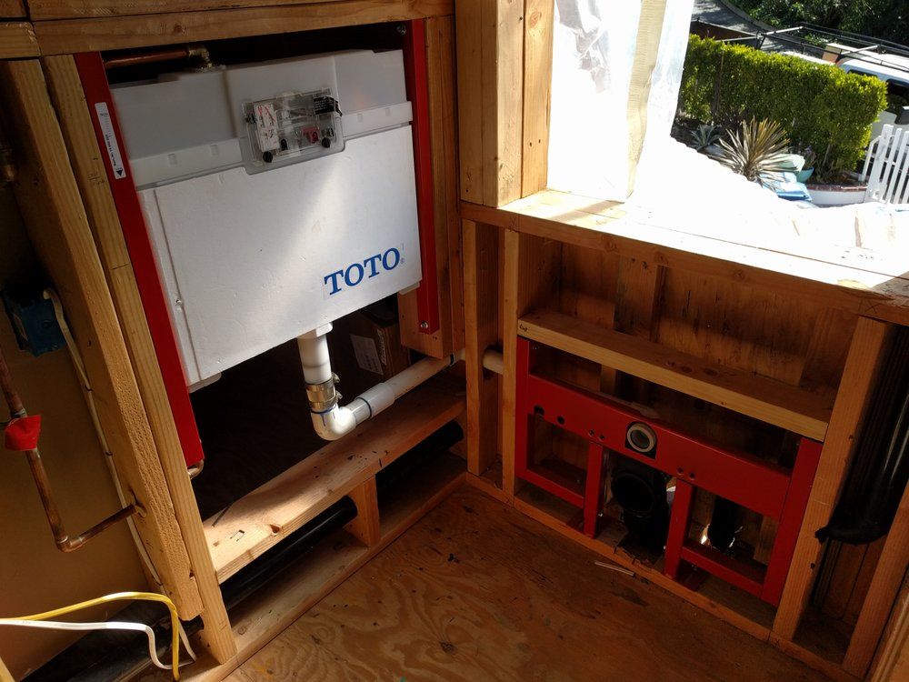 Framed-out wall with a TOTO toilet tank, plumbing, and unfinished construction. Red frame with a window to the right.