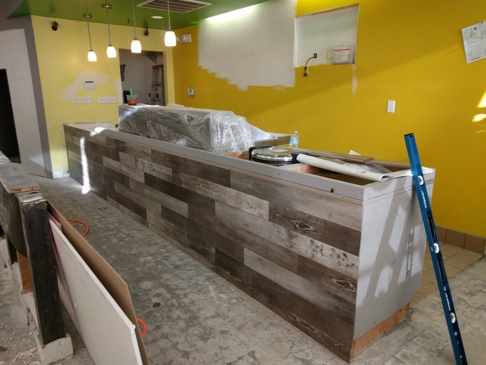 Restaurant interior under construction. Wood-paneled counter, yellow walls, unfinished floor.