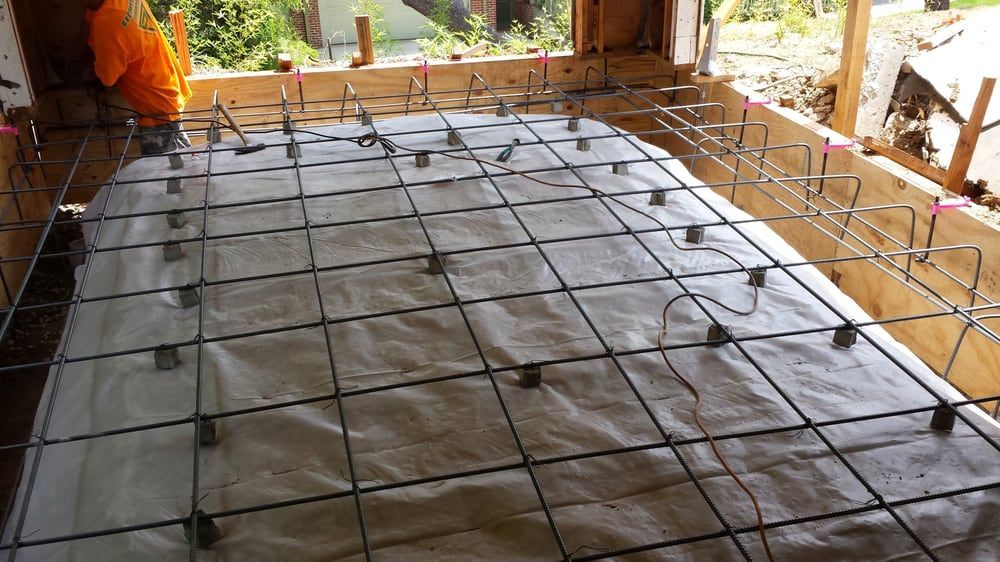 Construction site: Metal rebar grid laid over white fabric inside a wooden frame, ready for concrete pouring.