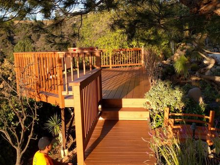Wooden deck in a lush garden with steps, railings, and a person in an orange shirt.