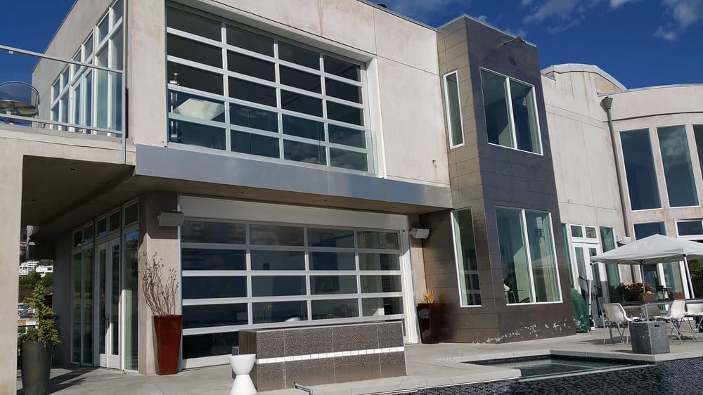 Modern house exterior with large glass garage door, windows, and patio. Blue sky.