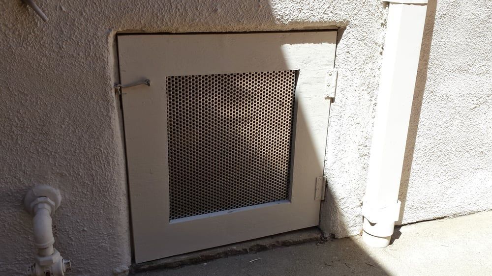 White door with metal mesh panel set into stucco wall, outdoors.