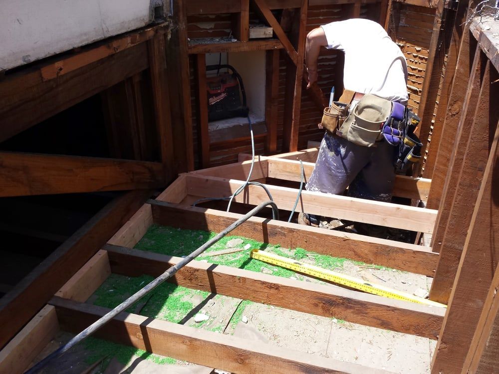 Construction worker building stairs with exposed wooden frame. Green material lines the steps, and tools are visible.