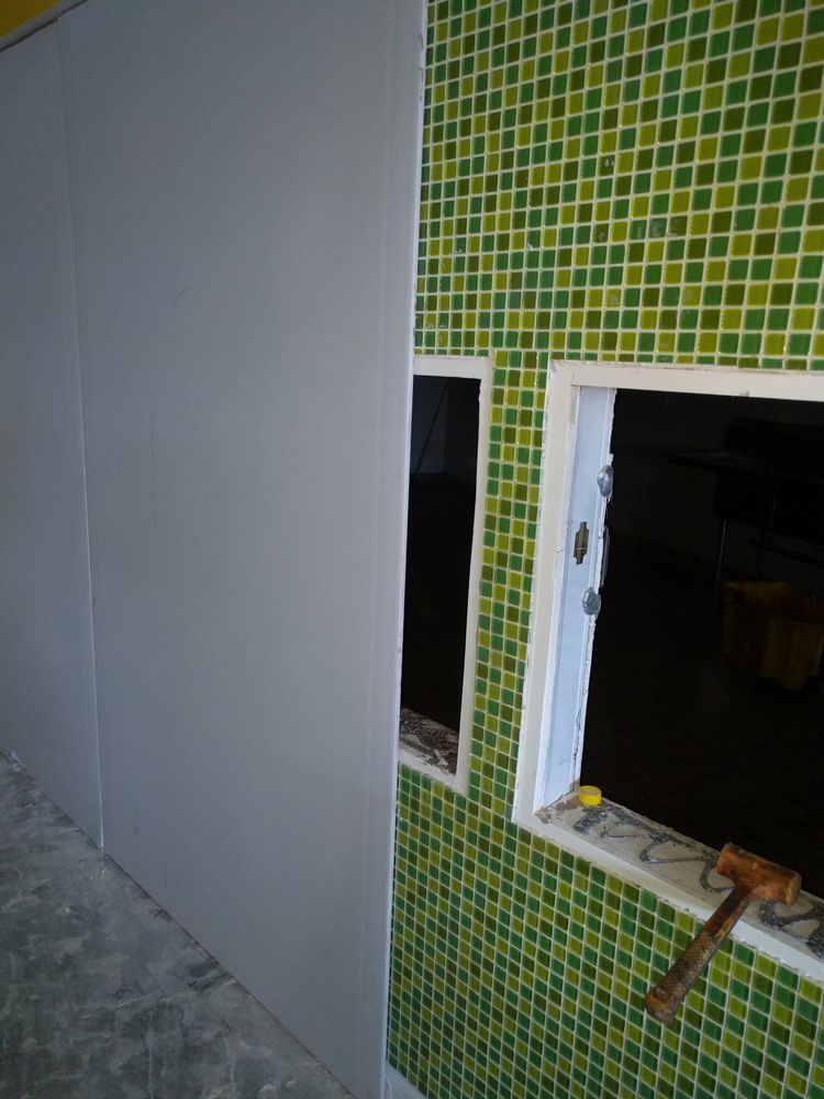 Gray wall paneling installed next to a wall with green and yellow mosaic tiles; two window openings.