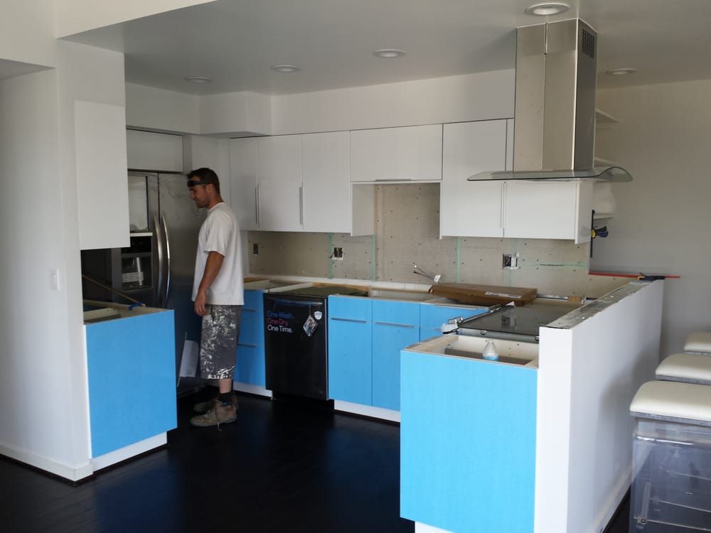 Person standing in a remodeled kitchen with blue and white cabinets, stainless steel appliances, and dark flooring.