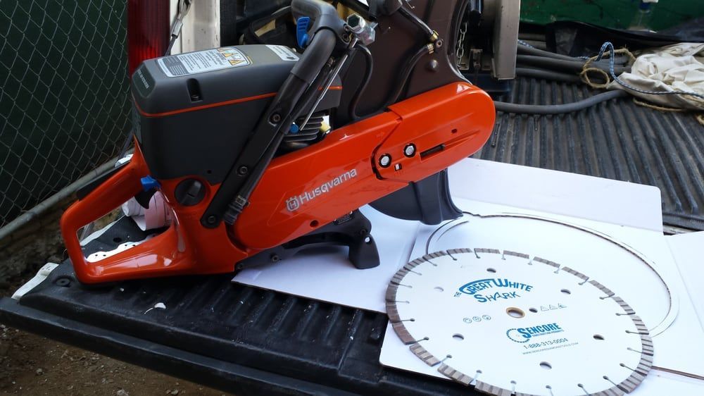 Orange Husqvarna concrete saw with a diamond blade on a truck bed.