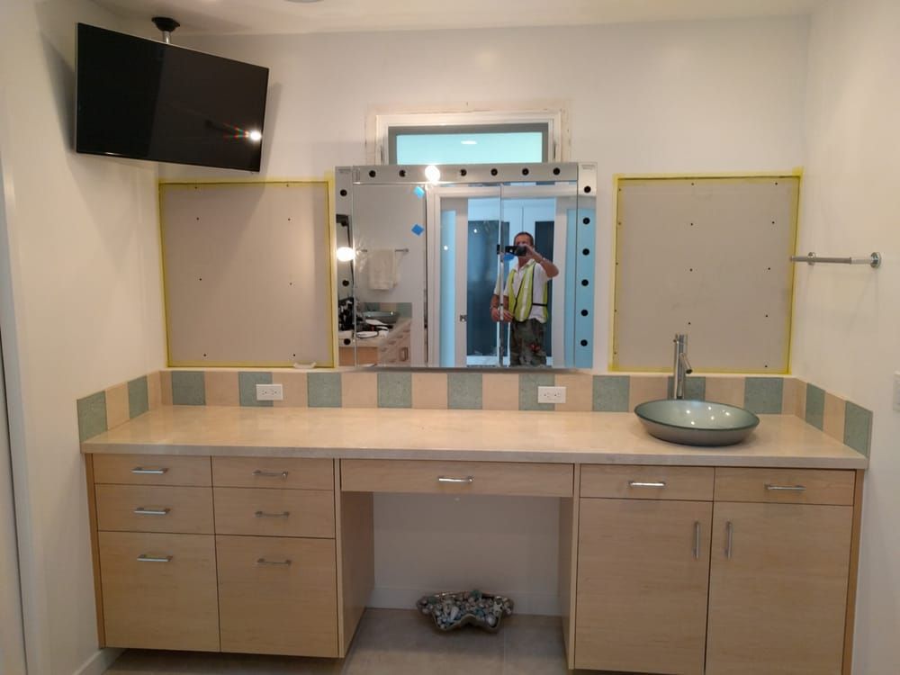 Bathroom with vanity, large central mirror, and TV. Beige cabinets and countertop, light blue and beige backsplash.