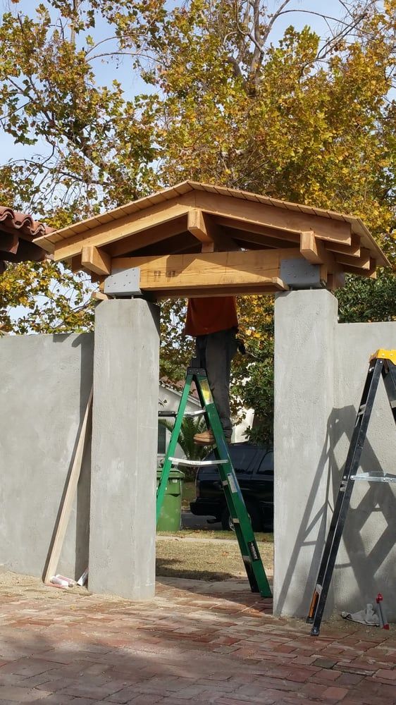 Person on a ladder working on a wooden roof over a concrete gate.