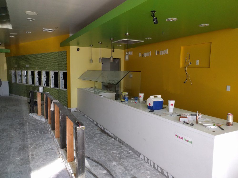 Empty store interior with yellow and green walls, white counter, unfinished flooring; construction phase.