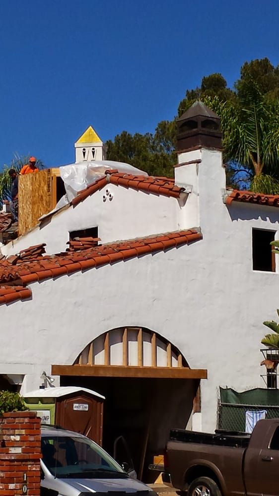 White stucco building with red tile roof, archway, chimney, and a yellow-topped dome. Sunny day.