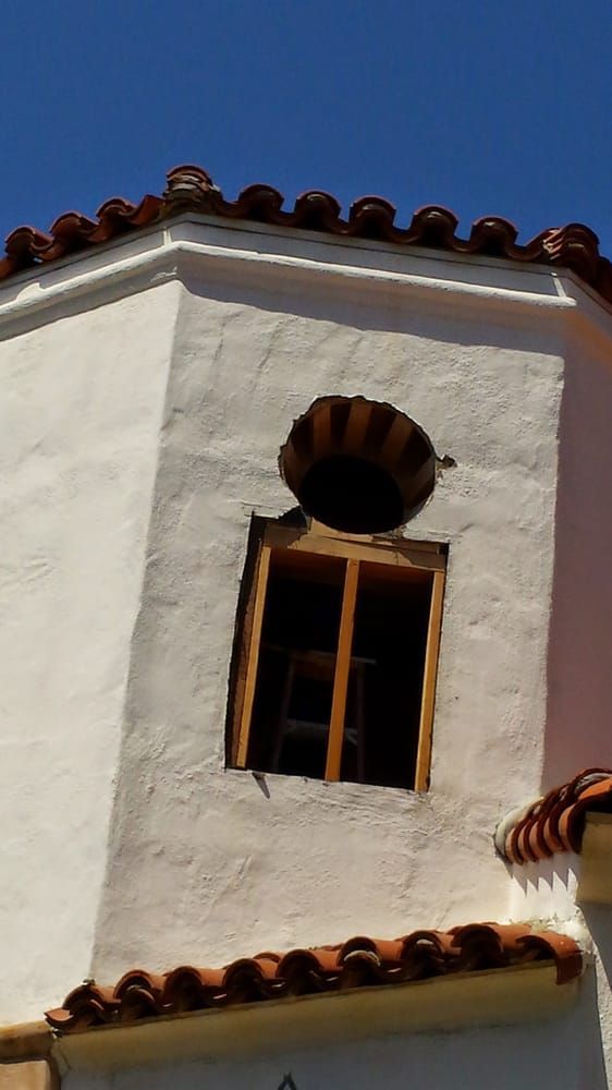 White stucco building with terracotta roof tiles and a window with a decorative top feature under a clear blue sky.