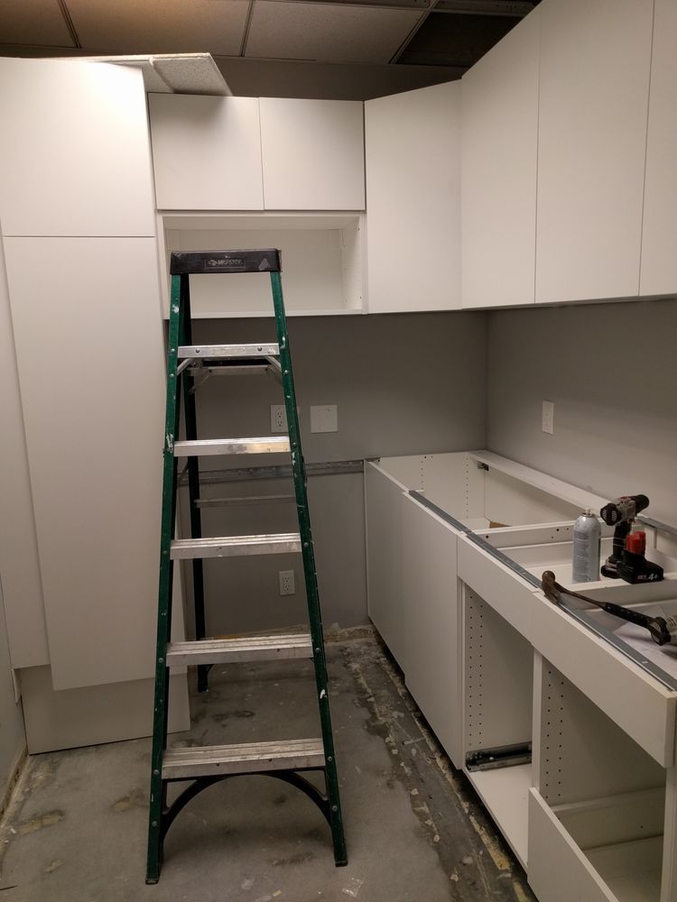 A mostly white kitchen under construction, with a green ladder.