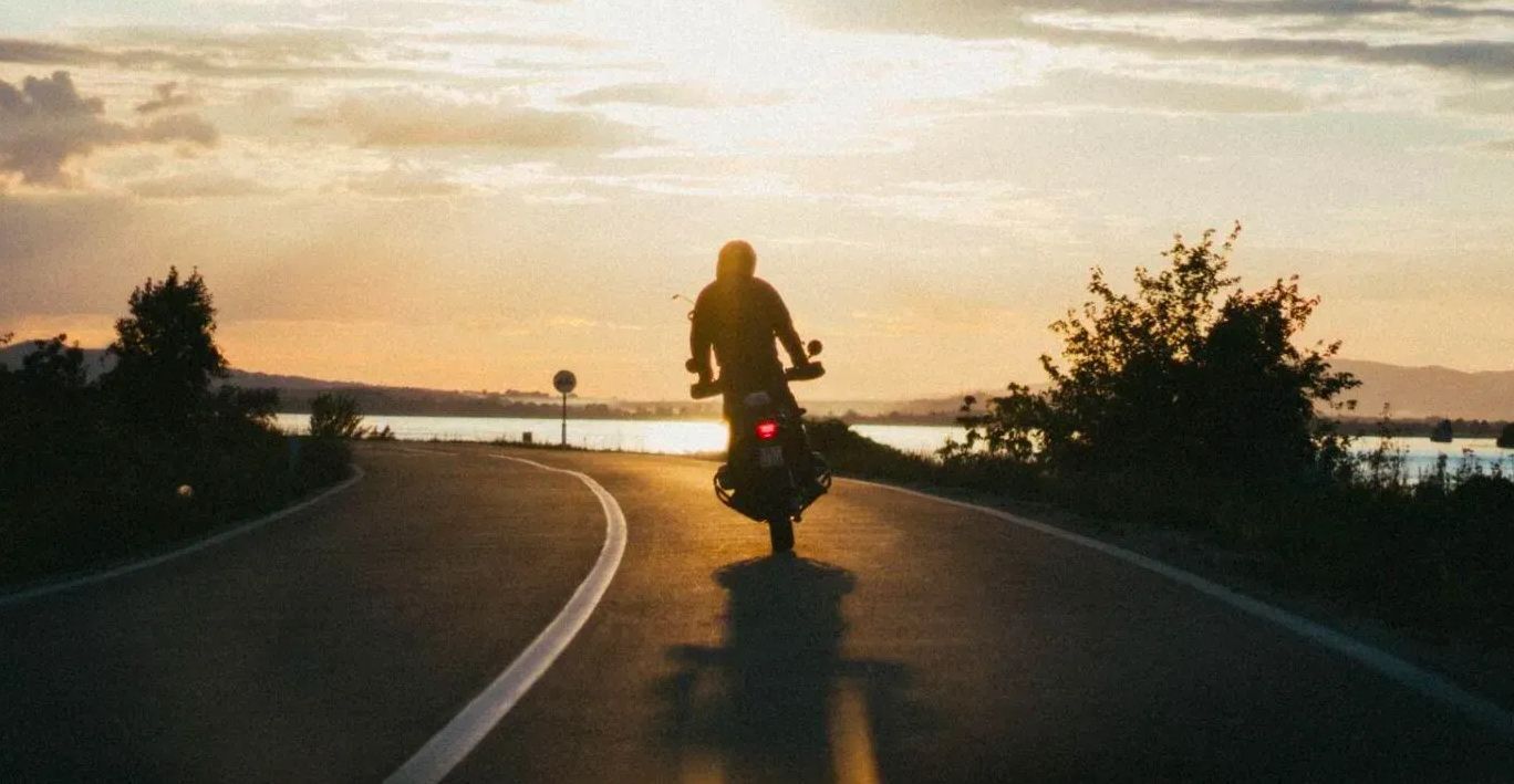 A man is riding a motorcycle down a road at sunset.
