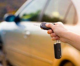 A person is holding a car key in front of a car.