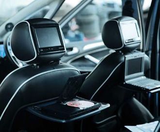 Car interior with screens mounted on the back of the front headrests and portable DVD players open on fold-down trays.