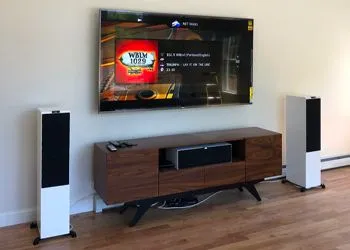 Living room with a large TV, speakers, and a media console.