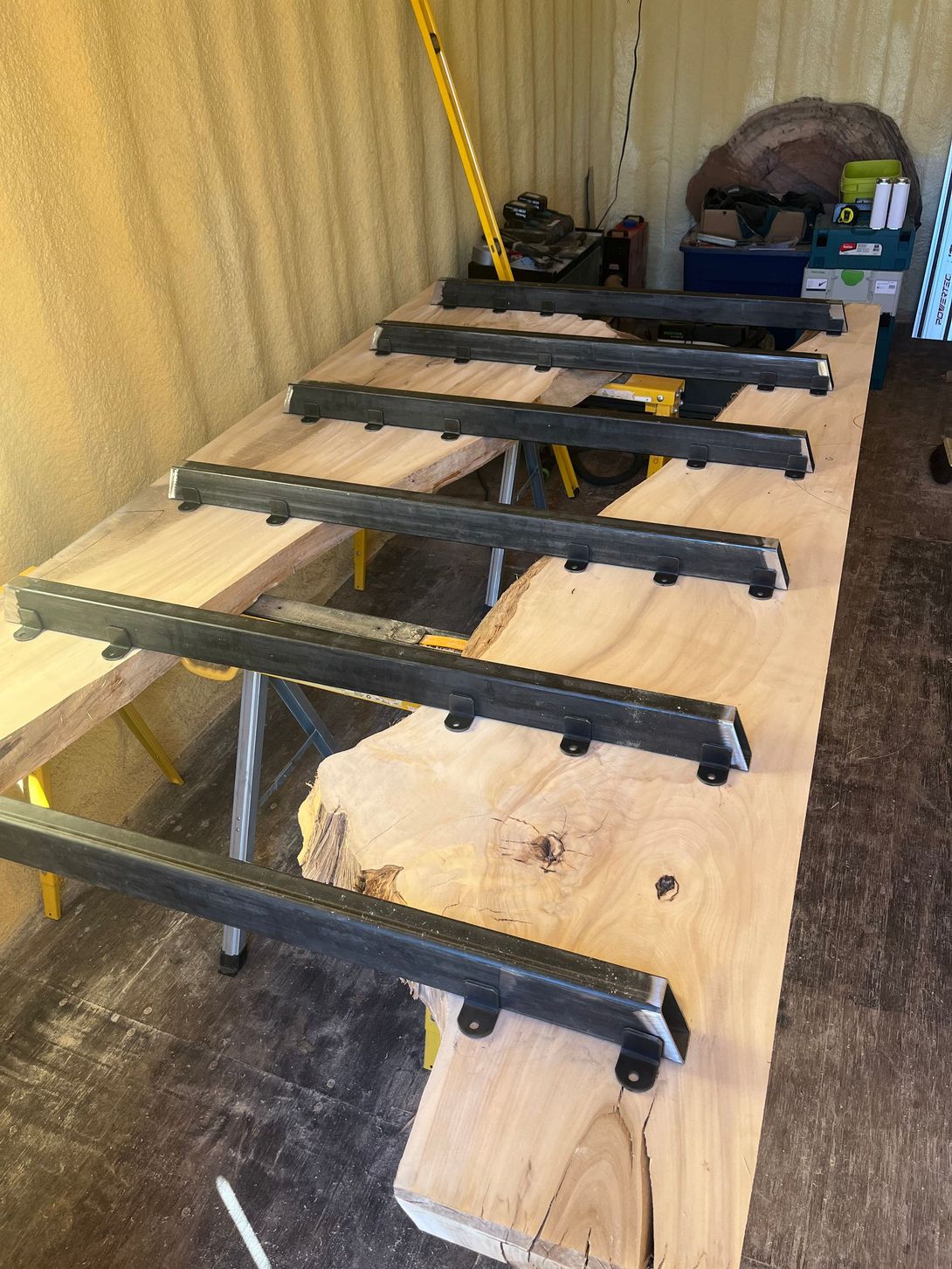 A large wooden slab with clamps, resting on sawhorses, inside a workshop.
