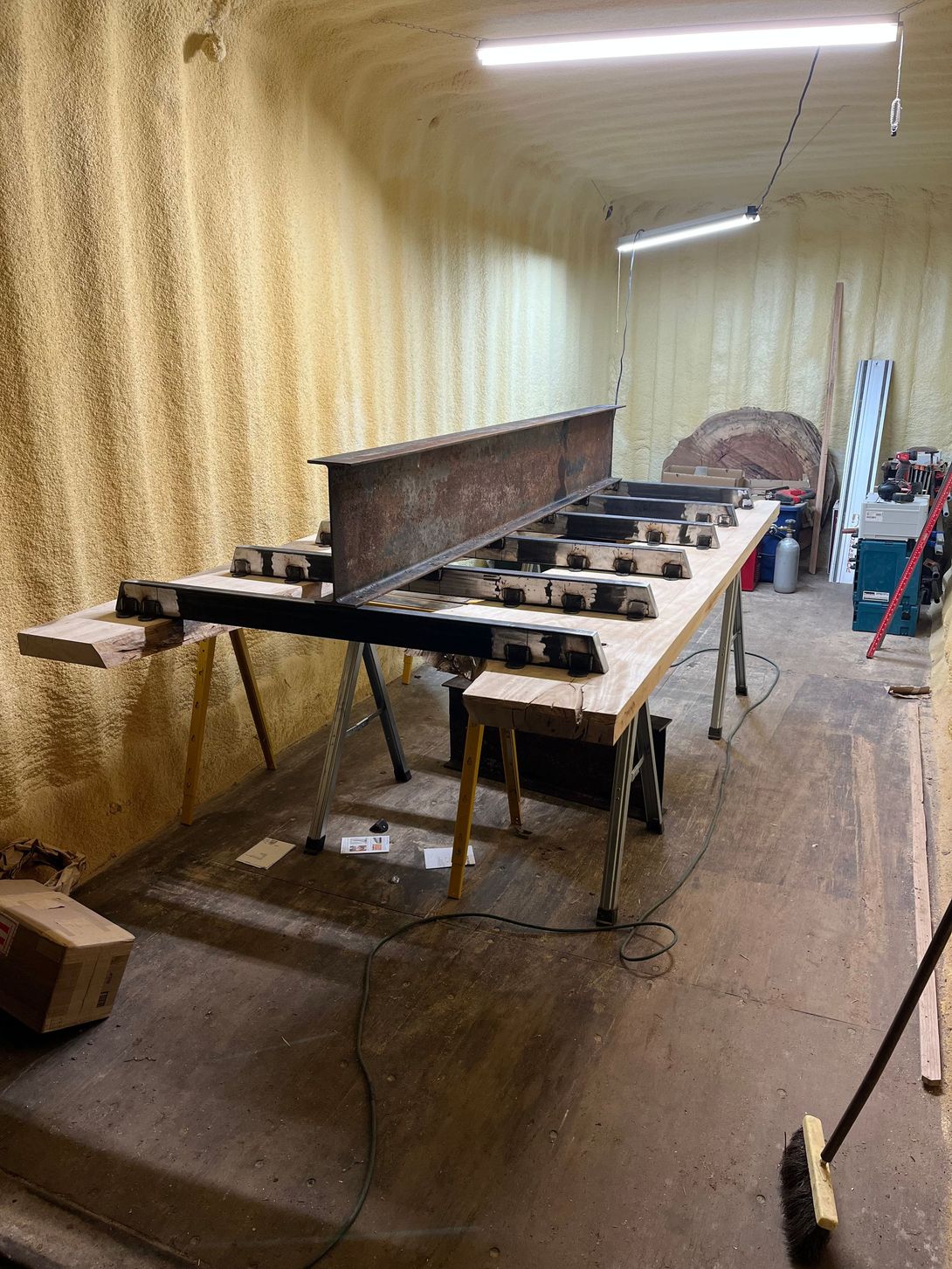 A work-in-progress workshop scene; a large metal beam atop a wooden structure on sawhorses.