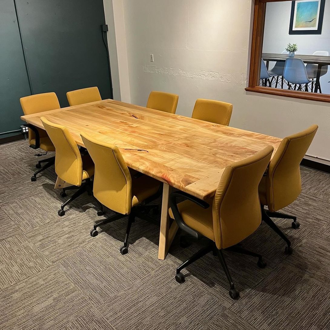 A conference room with a large wooden table and eight yellow chairs.