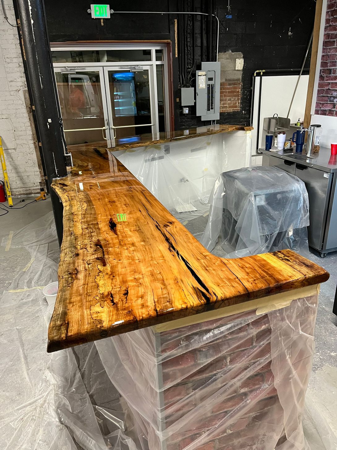 L-shaped wooden bar with glossy finish, in a partially constructed commercial space.