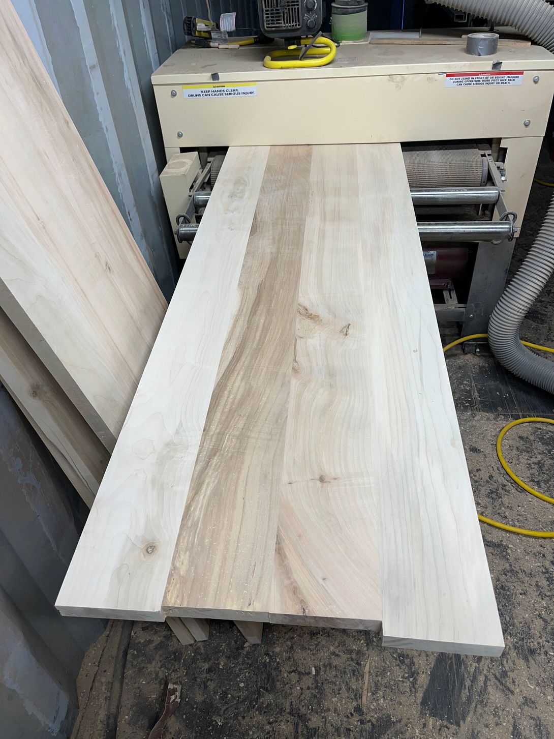 A wood plank being processed by a wide belt sander in a workshop setting.