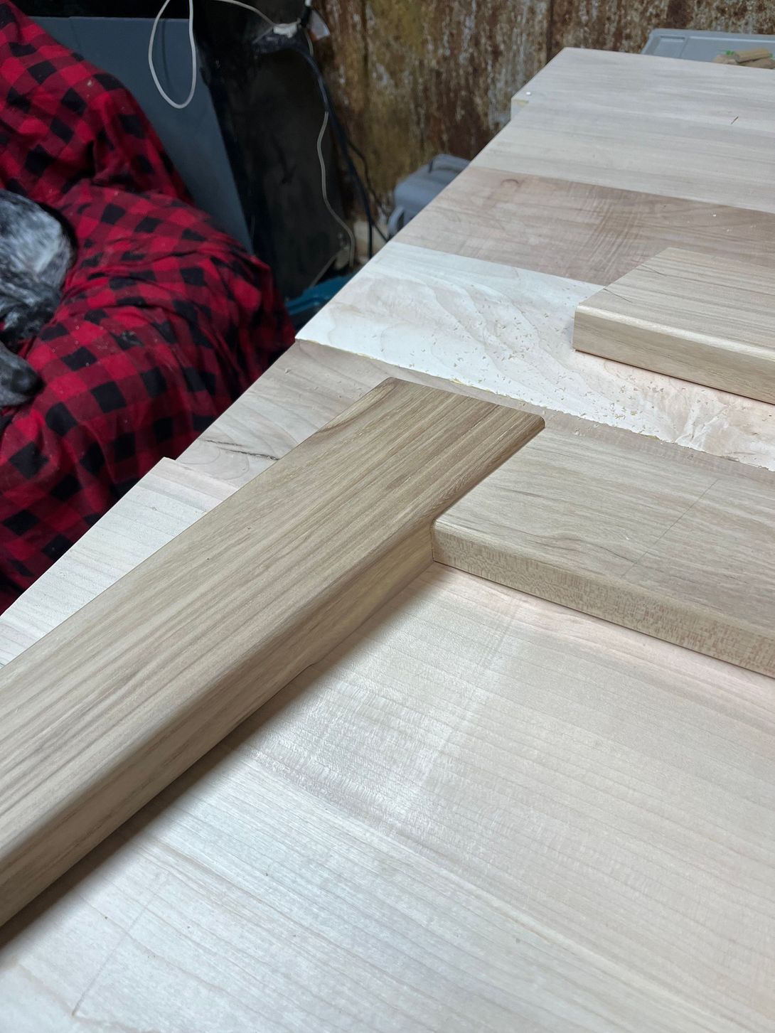 Wood pieces laid out on a light wood surface, likely for a woodworking project, with a plaid blanket in the background.