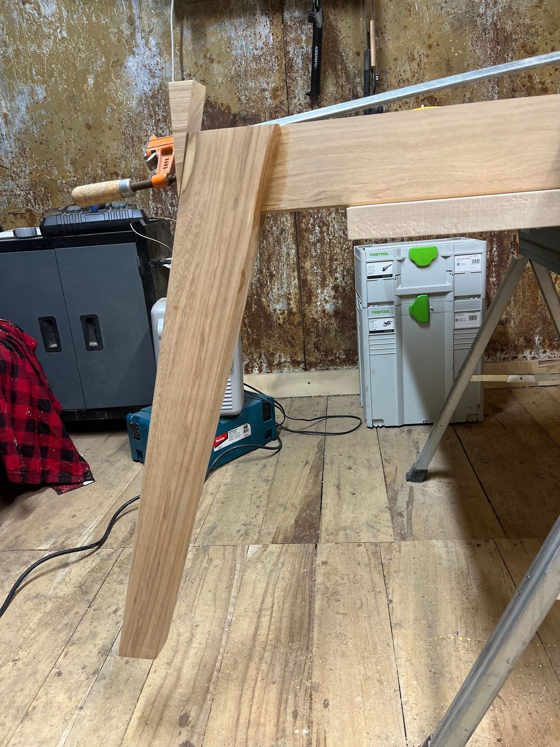 Wooden table leg being built in a workshop, light brown wood against a cluttered background.