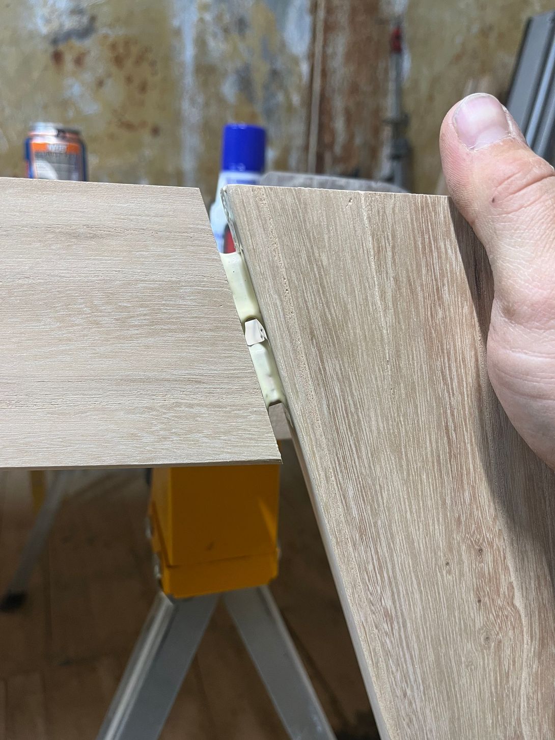 Two wooden planks being joined, held by a hand, against a background of a work area.