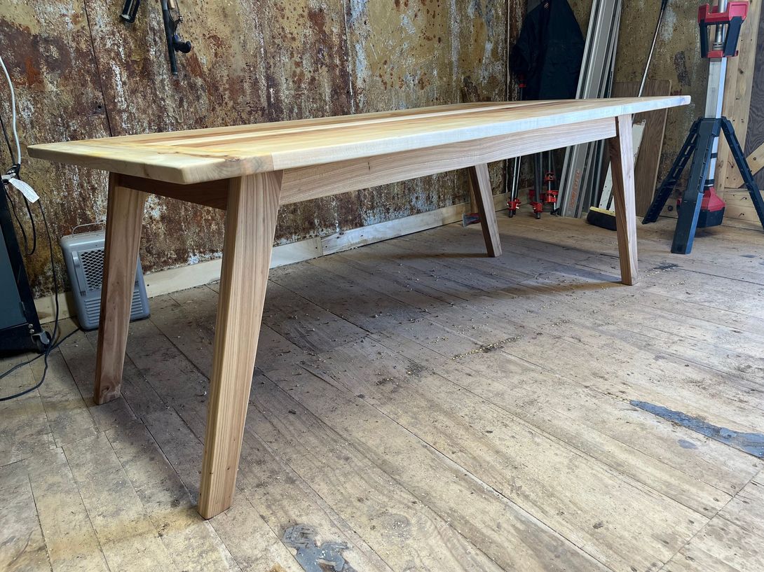 Wooden table with angled legs, on a wooden floor, against a weathered wall.