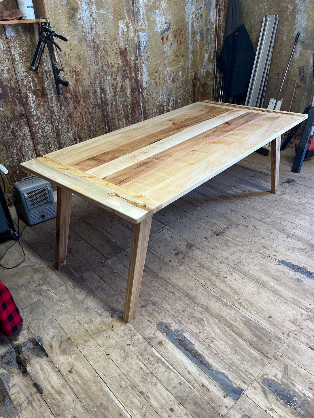 Wooden dining table with a light brown top and angled legs, indoors.