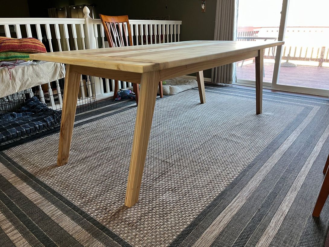 Wooden dining table on a patterned rug, near a railing and a sliding glass door.