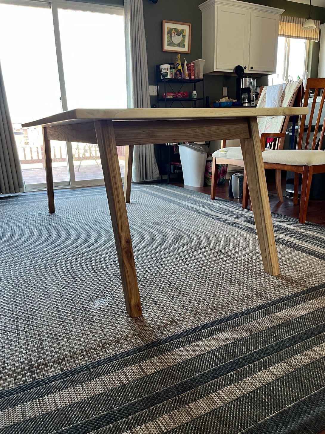 Wooden table with angled legs on a patterned rug in a home setting.