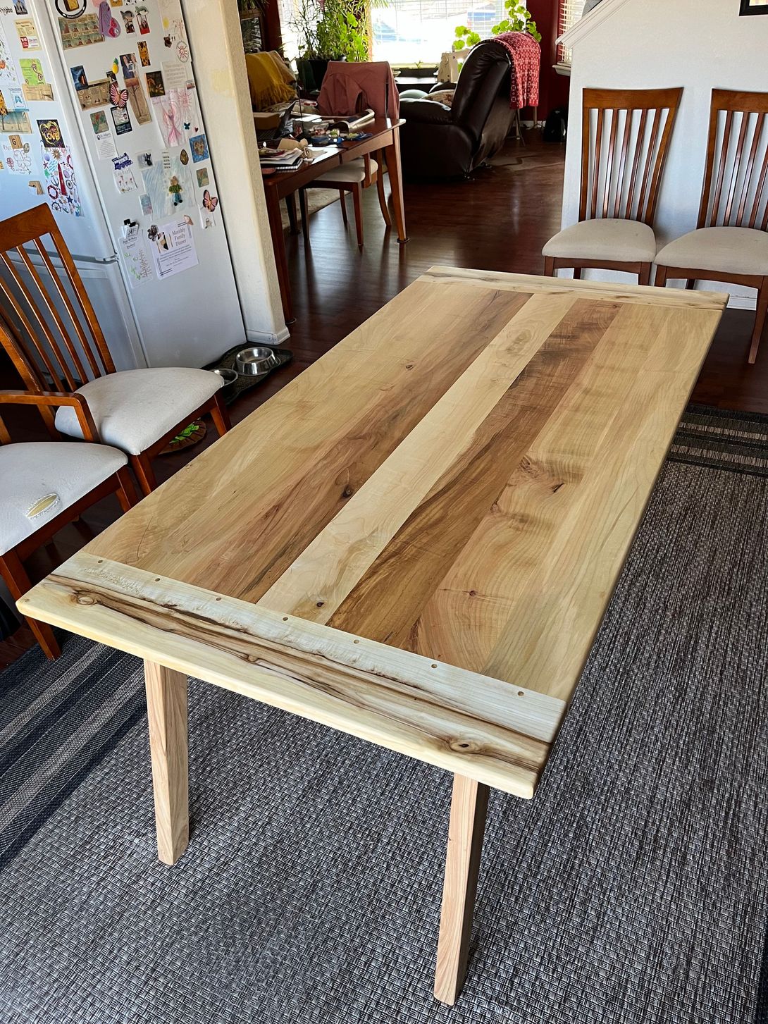Wooden dining table with light-colored wood top, set on light-colored legs, in a brightly lit room.