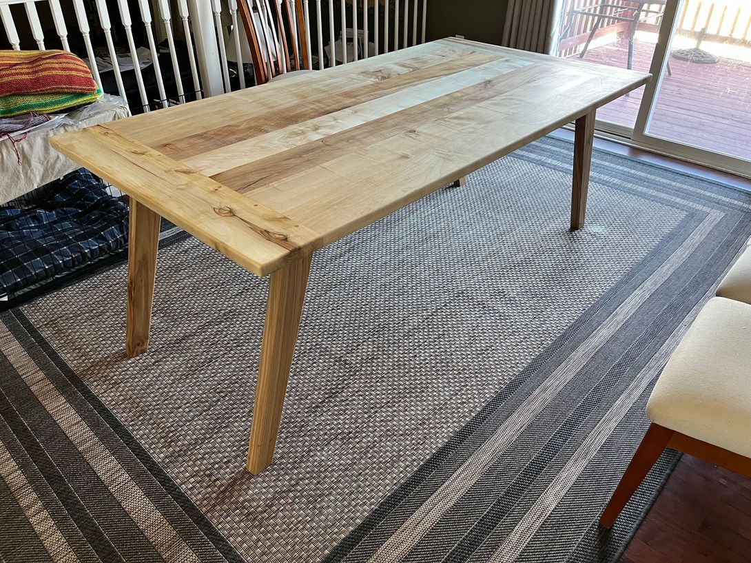 Wooden dining table with four tapered legs, on a patterned rug.