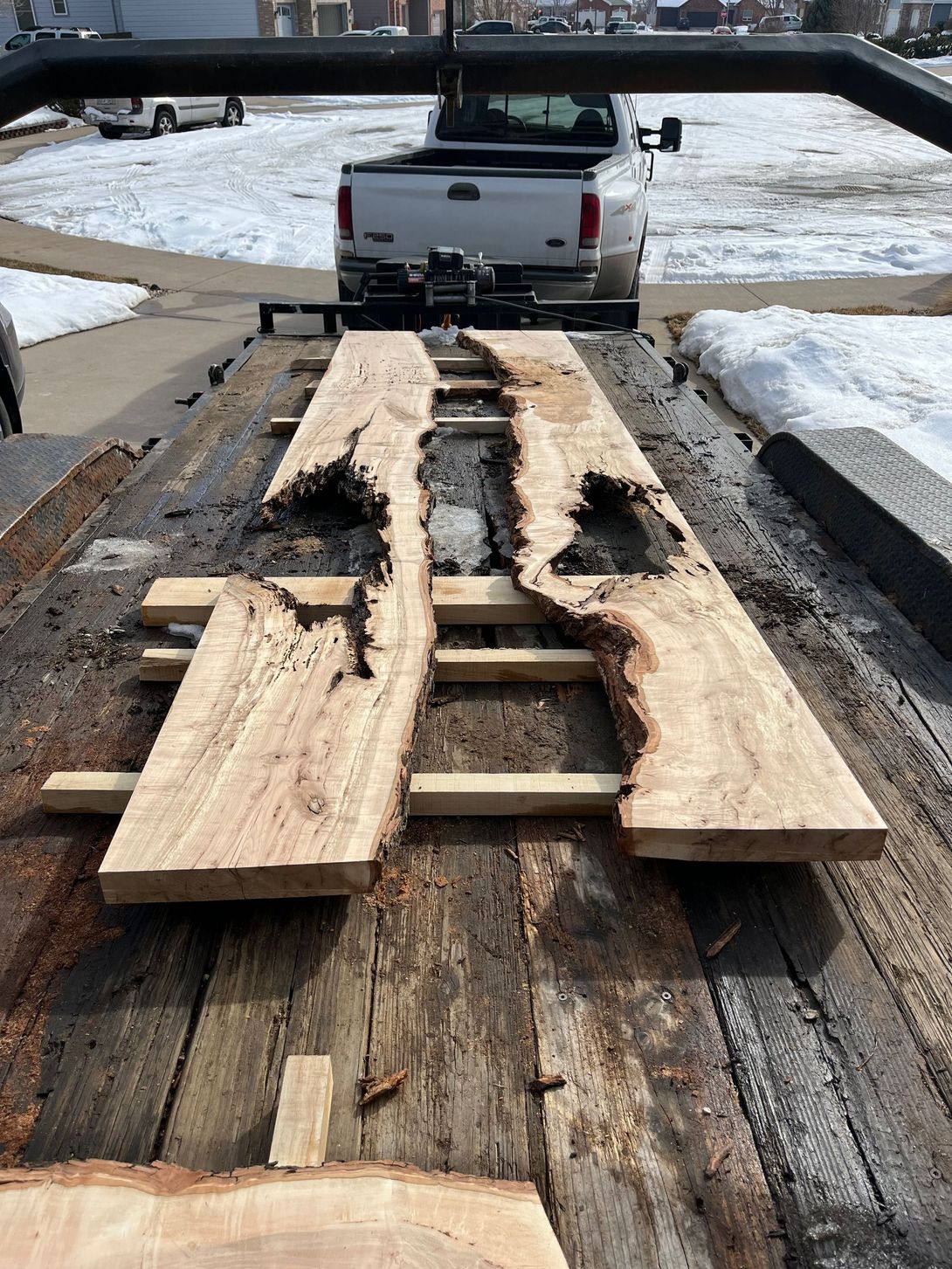 Two live edge wood slabs with black voids on a trailer, truck in background.