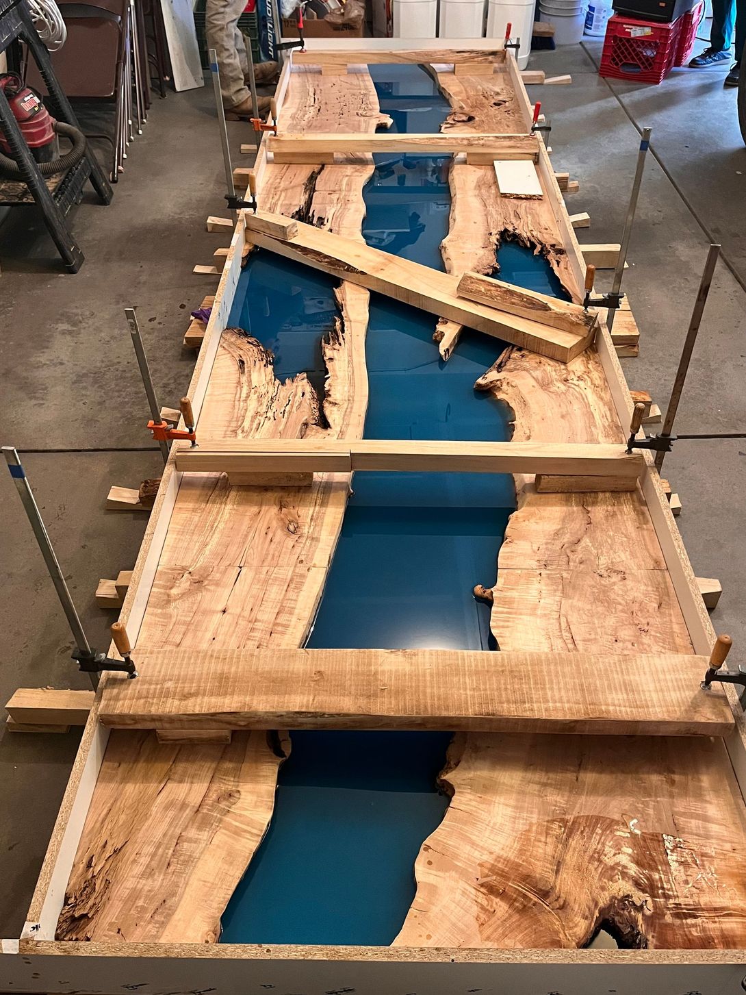 Wooden table tops with blue resin river design being clamped in place for curing.