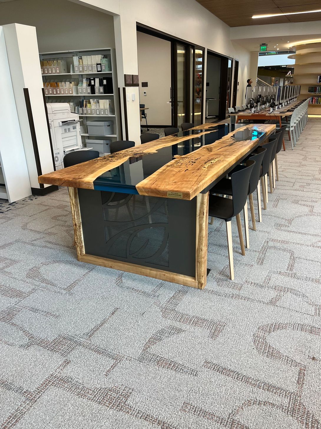 A long, wooden table with black chairs in a modern setting, with textured flooring and a glass door.