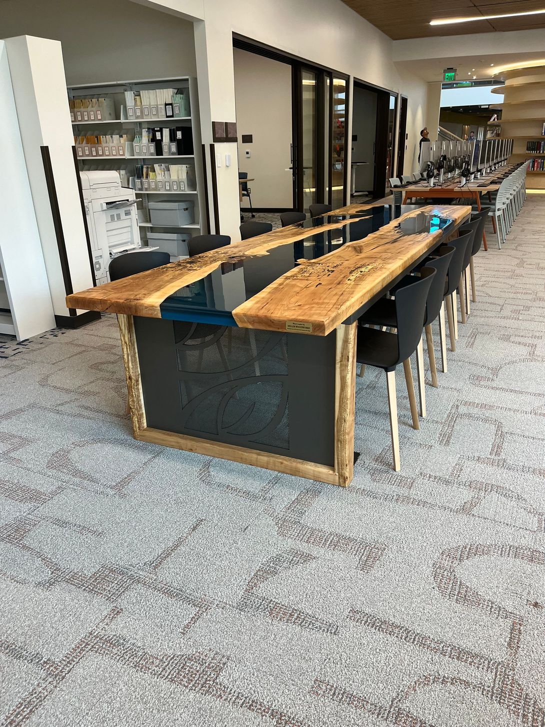 Long wooden table with blue resin center in a library setting.