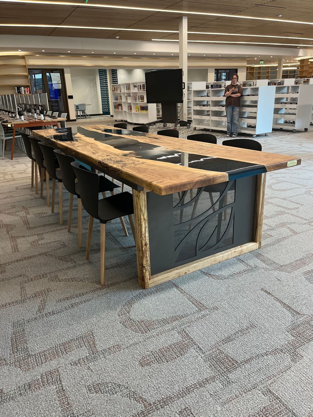 Long wooden table with black chairs, in a library setting.