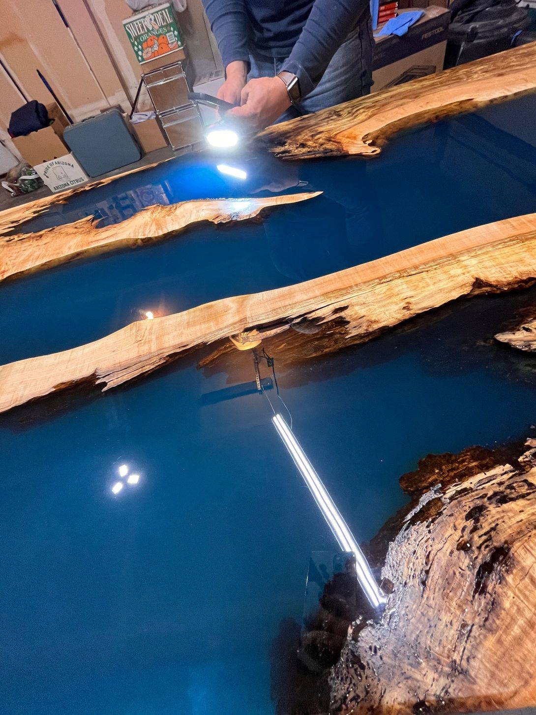 Blue epoxy river table with wooden edges, a person using a light to inspect the surface.