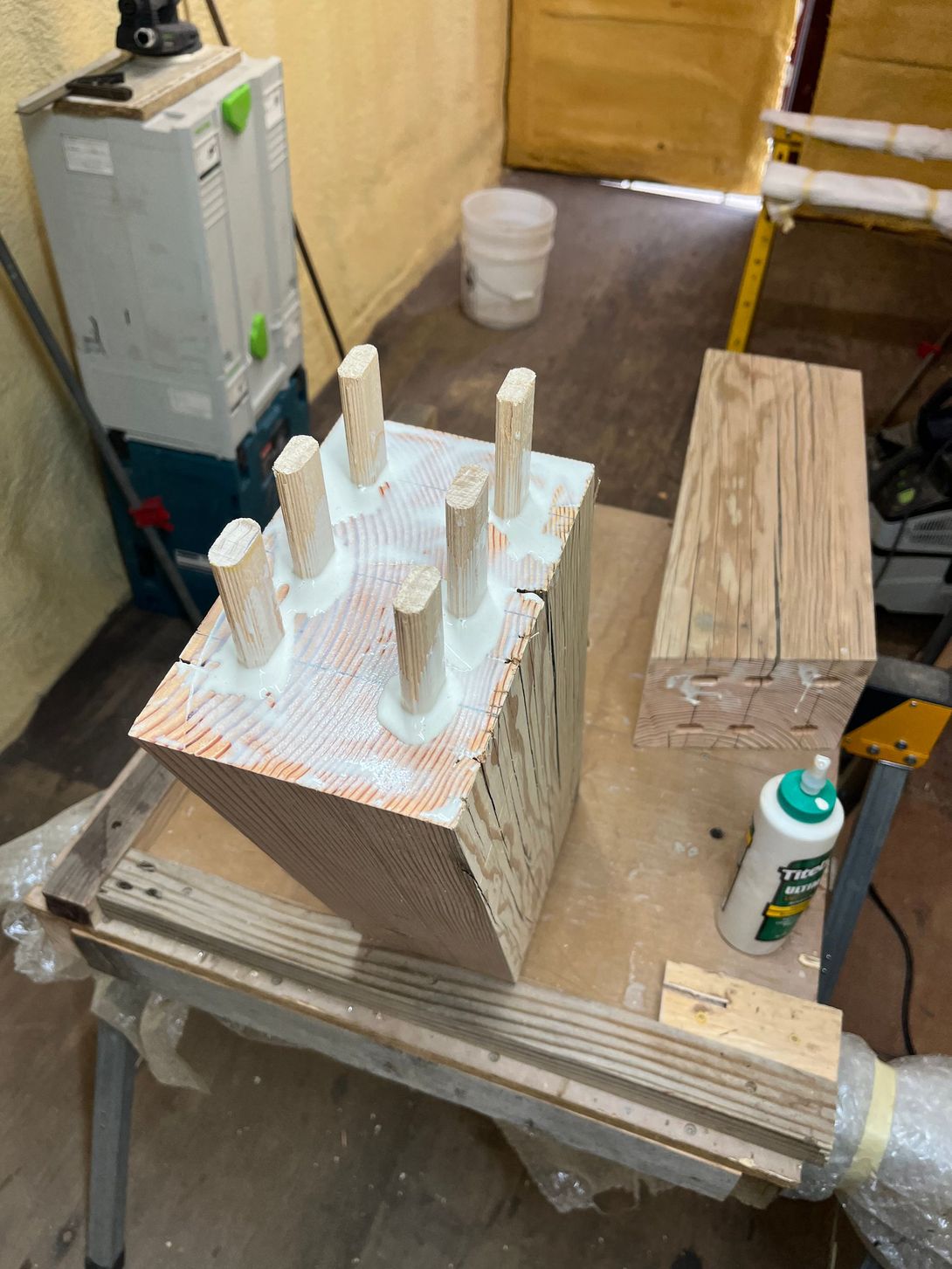 Wooden blocks with glue, dowels, and a glue bottle on a workbench.