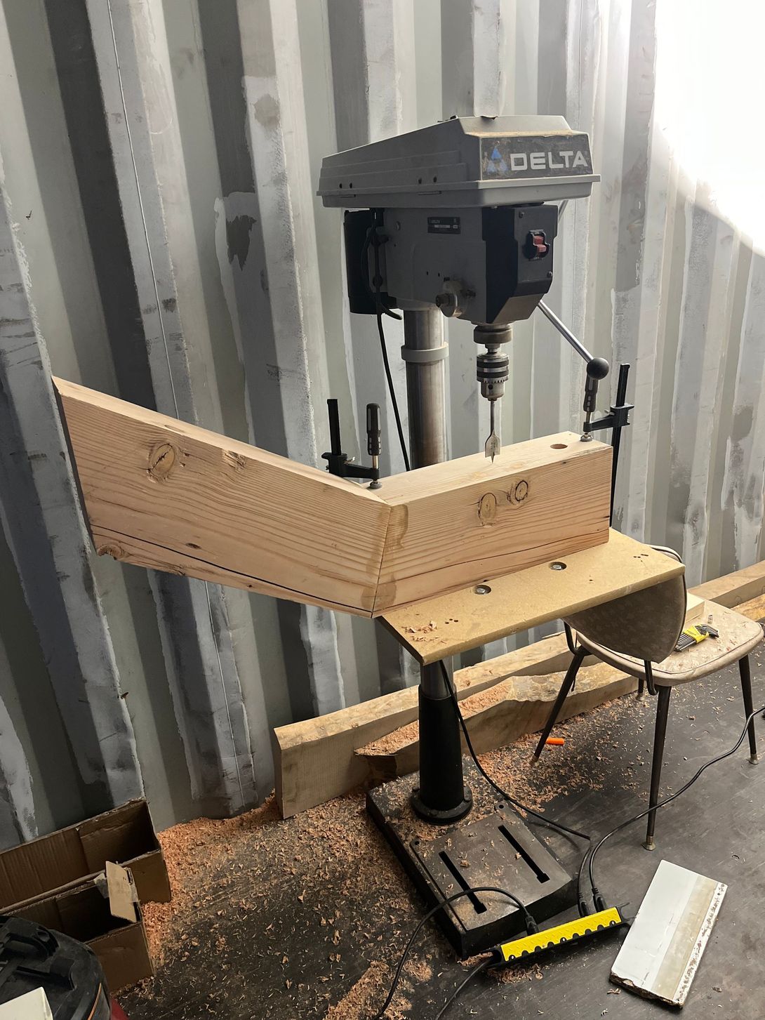 A drill press drilling a wooden piece in a workshop setting.