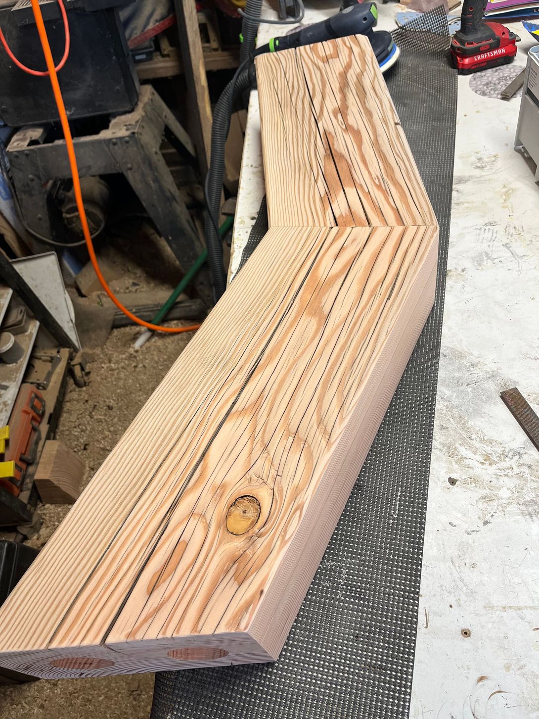 Two angled wooden beams with visible grain and knot, in a workshop setting.
